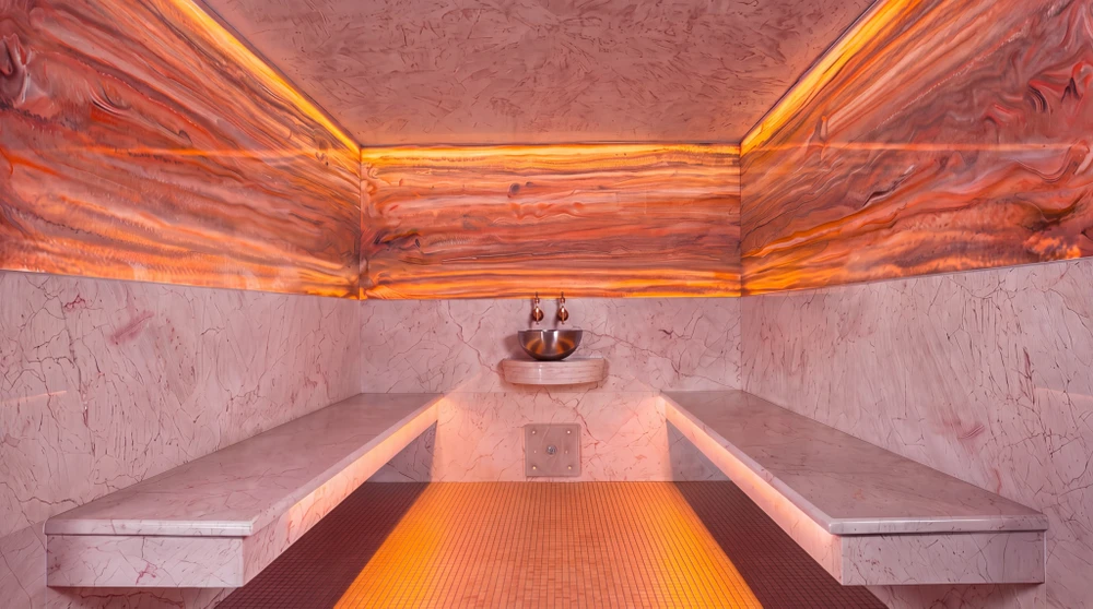 Sauna finlandais avec bancs en bois de cèdre à lattes, mur décoratif en briques de sel de l'Himalaya rose-orangé rétroéclairées