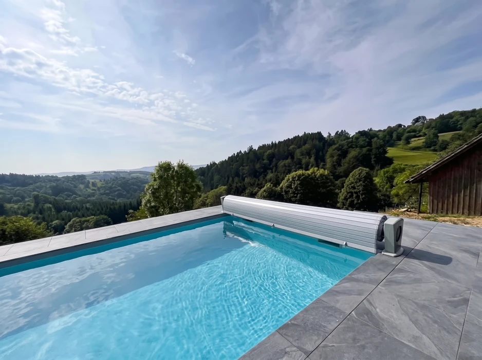 Jardin extérieur résidentiel avec piscine couverte d'une bâche de protection enroulable noire, montée sur un axe tubulaire aluminium avec enrouleur motorisé