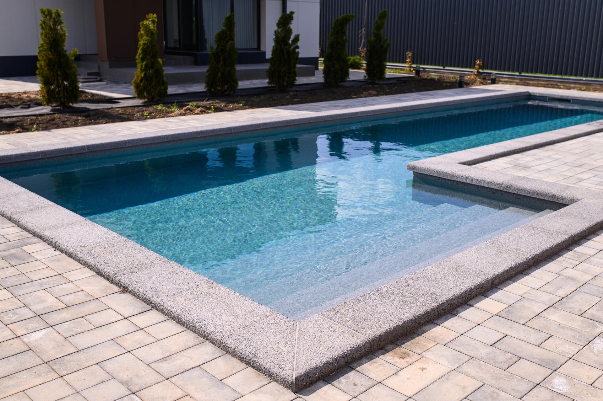 Piscine extérieure avec lame d'eau en inox montée sur un mur en pierre travertin appareillée en opus incertum
